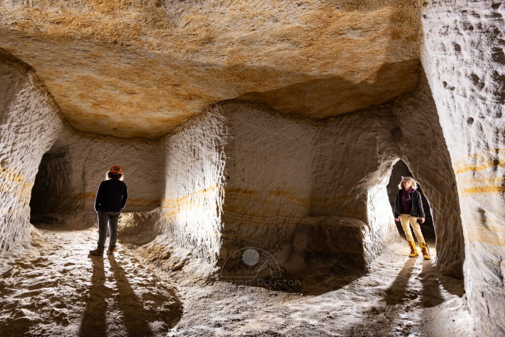 Galeries creusées dans le sable avec deux spéléologues. Par endroit la couche de sable est de couleur ocre. (Tout comme le plafond). (Carrière de Saint-Pancrace, Gard)