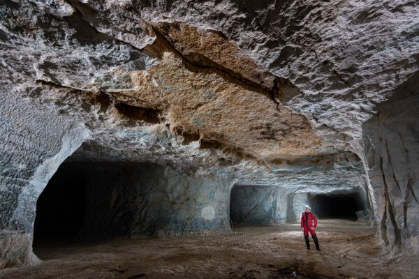 Un partie du plafond s'est effondrée, effaçant la coloration bleue (Un spéléo en combinaison rouge regarde le plafond). (Carrière de Vallabrègues, Vaucluse)