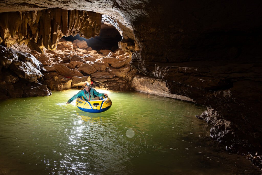 Un spéléo dans un bateau pneumatique essaye d'avancer en utilisant ses mains comme rame. (Évent de Foussoubie, Ardèche)