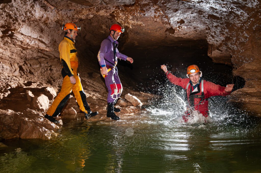 Deux spéléo regardent, un troisième fait jaillir de l'eau en courant. Dans le siphon de l'Évent de Foussoubie. (Évent de Foussoubie, Ardèche)