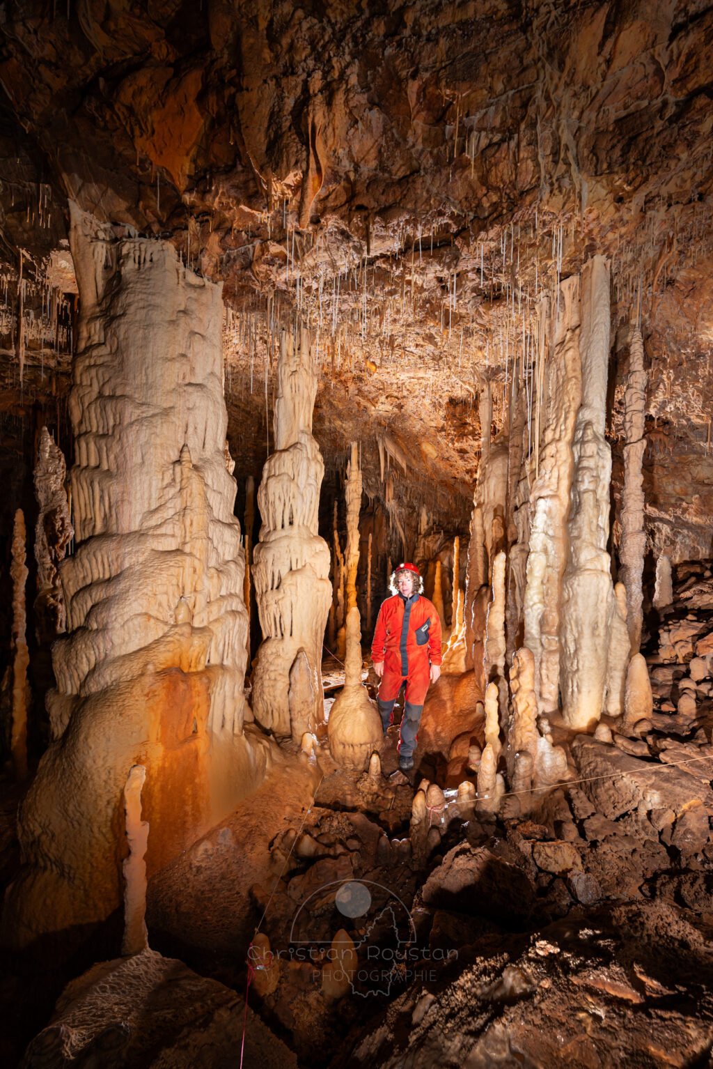 Dans la grande salle de la grotte Flandin, un spéléo se trouve entre deux grands massifs de concrétions. (Grotte Flandin, Ardèche)