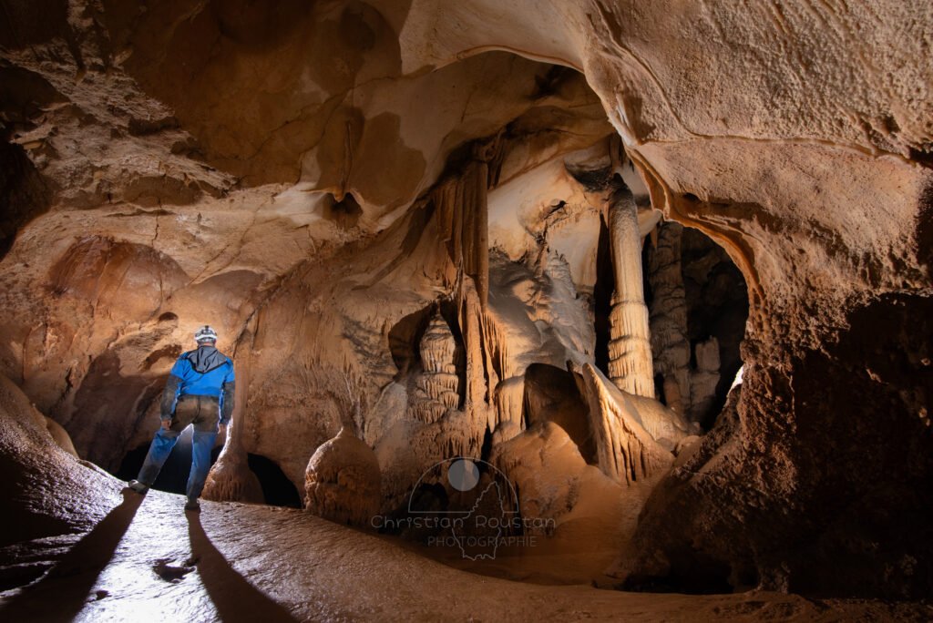 Fenêtre sur la grande salle du Barry avec un seul spéléologue en bleu. (Grotte du Barry, Gard)