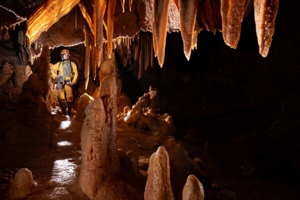 Un spéléo en arrière d'une zone très concrétionnée. (Aven Grotte de l'Émeraude, Gard)