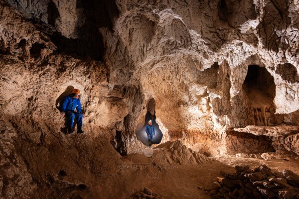 Deux spéléo sur la gauche, on remarque le plancher sur la droite qui donne un aperçu de la hauteur du creusement (Grotte de Louoï, Ardèche)