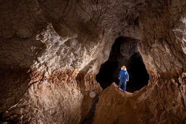 Le niveau de creusement est bien visible, spéléo en bleu dans la galerie (Grotte de Louoï, Ardèche)