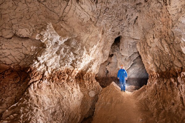 Le niveau de creusement est bien visible, spéléo en bleu dans la galerie (Grotte de Louoï, Ardèche)