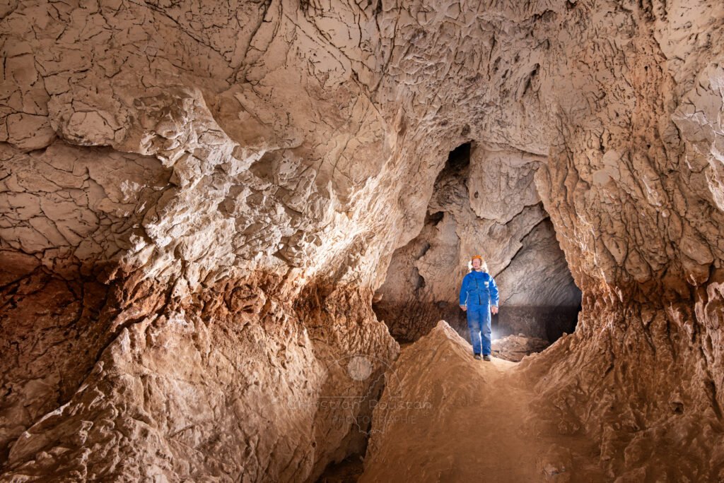 Le niveau de creusement est bien visible, spéléo en bleu dans la galerie (Grotte de Louoï, Ardèche)