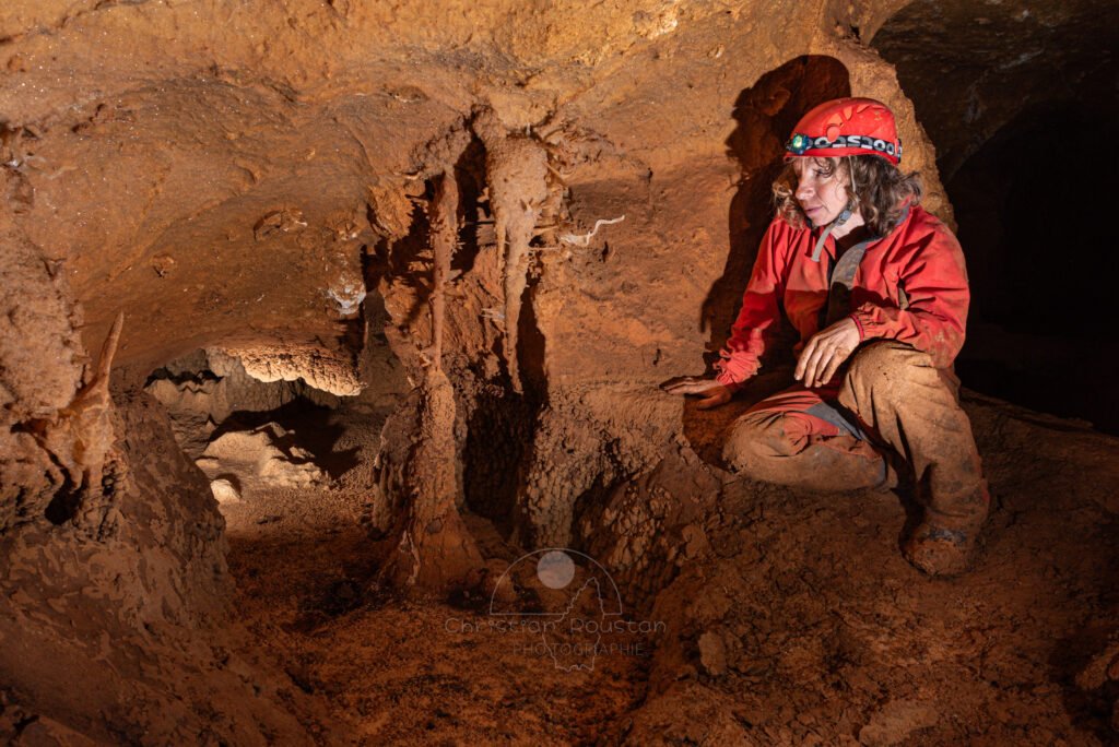 Spéléo au bord d'un gour regarde une fine excentrique blanche (Spéléothème, Grotte de l'interrogation, Gard)