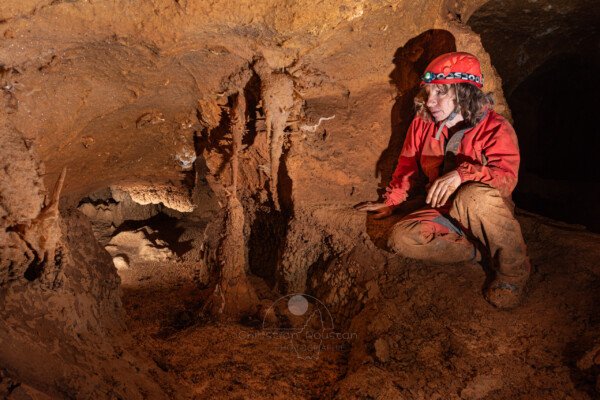 Spéléo au bord d'un gour regarde une fine excentrique blanche (Spéléothème, Grotte de l'interrogation, Gard)
