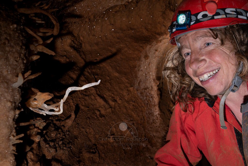 Spéléo souriante regarde une fine excentrique blanche (Spéléothème, Grotte de l'interrogation, Gard)