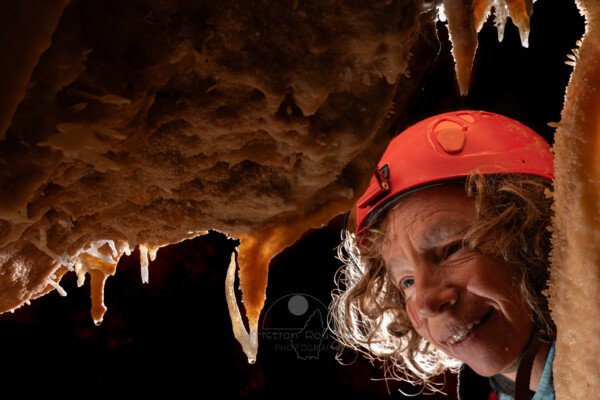 Une spéléo regarde une petite excentrique en forme de harpon (Spéléothème, Grotte de l'interrogation, Gard)
