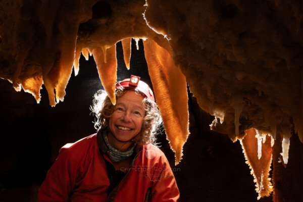 Une spéléologue derrière le rideau de concrétions (Spéléothème, Grotte de l'interrogation, Gard)