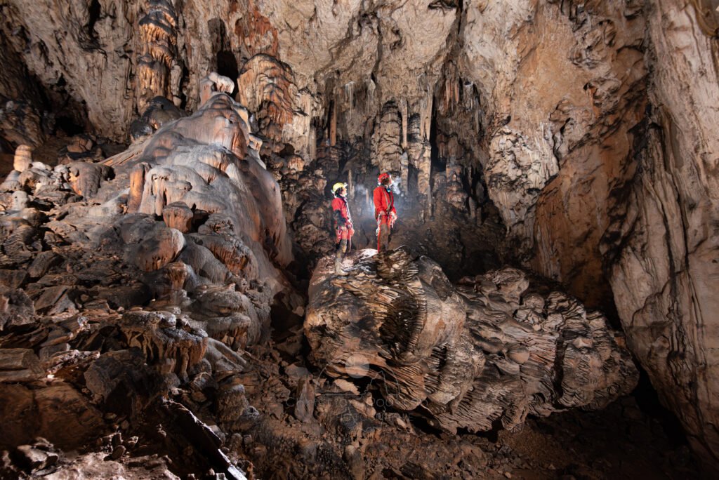Deux spéléologues dans la première salle avec le grand pilier effondré (Aven Grotte Nouvelle, Ardèche)