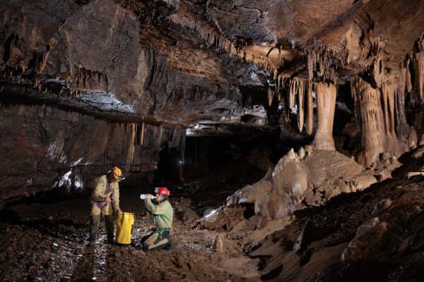 Deux spéléos à coté d'un massif de concrétions. (Réseau de la Cocalière, Résurgence de la Cotepatière, Aven de la Courcalhère, Ardèche)