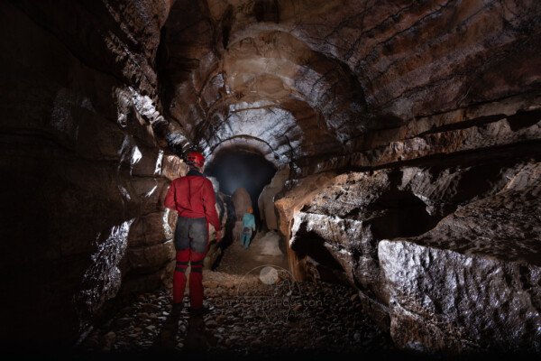 Une grande galerie en forme de trou de serrure, avec des spéléos. (Réseau de la Cocalière, Résurgence de la Cotepatière, Aven de la Courcalhère, Ardèche)