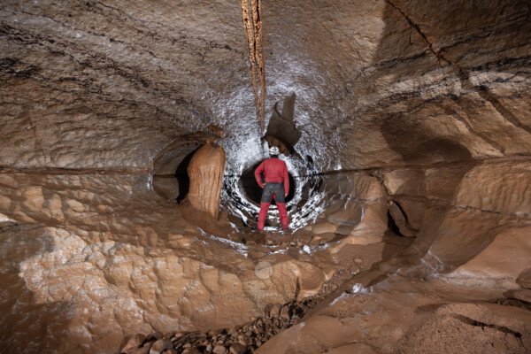 A gauche une rare concrétion dans la conduite forcée, avec spéléo au centre. (Réseau de la Cocalière, Résurgence de la Cotepatière, Aven de la Courcalhère, Ardèche)