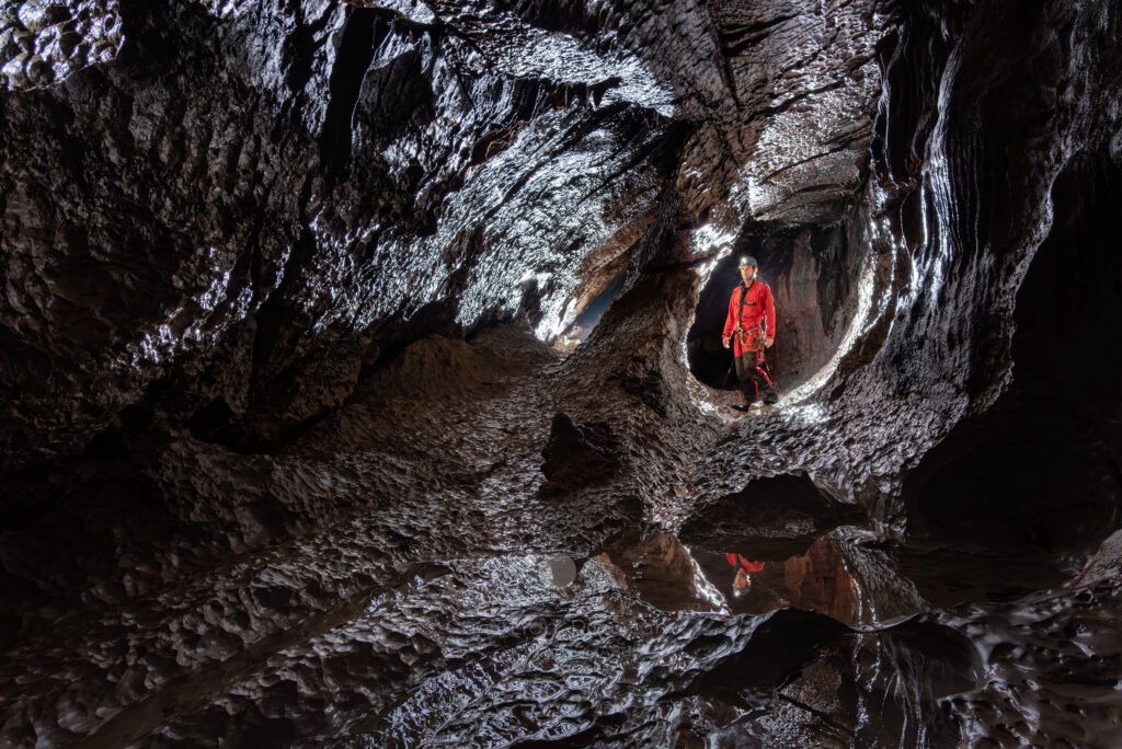 Spéléo dans dans galerie avec le reflet de sa tête dans un gour (Évent de Peyrejal, Ardèche)