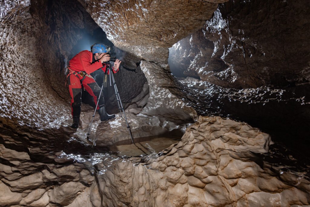 Le photographe en action, son appareil sur trépied dans galerie avec coups de gouges (Évent de Peyrejal, Ardèche)