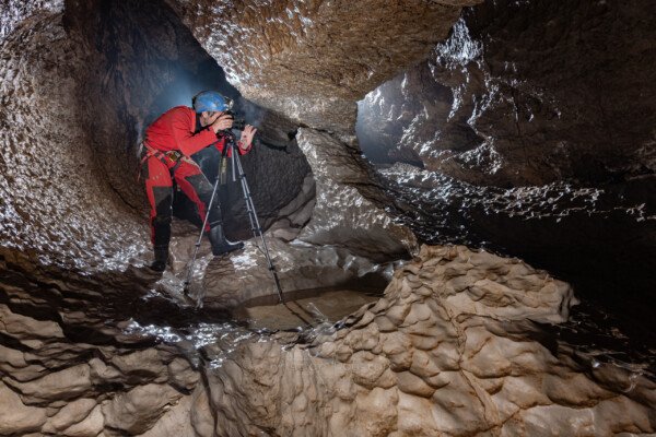 Le photographe en action, son appareil sur trépied dans galerie avec coups de gouges (Évent de Peyrejal, Ardèche)