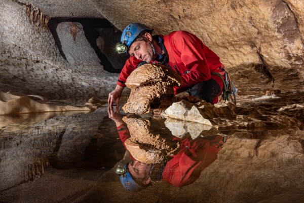 Reflet dans une marmite d'un spéléo et d'une concrétion en forme de champignon (Évent de Peyrejal, Ardèche)