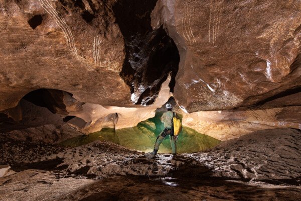 Un spéléo regarde la dernière vasque avant le siphon (Évent de Peyrejal, Ardèche)