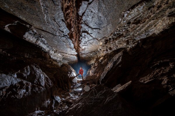 Un spéléo dans une belle galerie au plafond lisse coupé par une grosse fracture (Grotte de Pézenas, Ardèche)