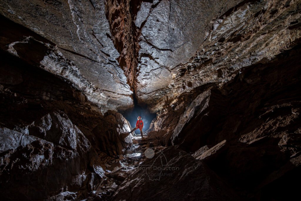 Un spéléo dans une belle galerie au plafond lisse coupé par une grosse fracture (Grotte de Pézenas, Ardèche)