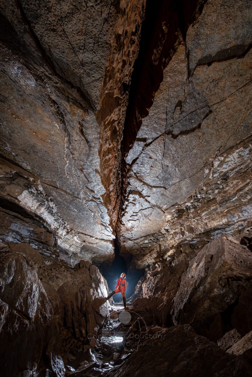 Un spéléo dans une belle galerie au plafond lisse coupé par une grosse fracture (Grotte de Pézenas, Ardèche)