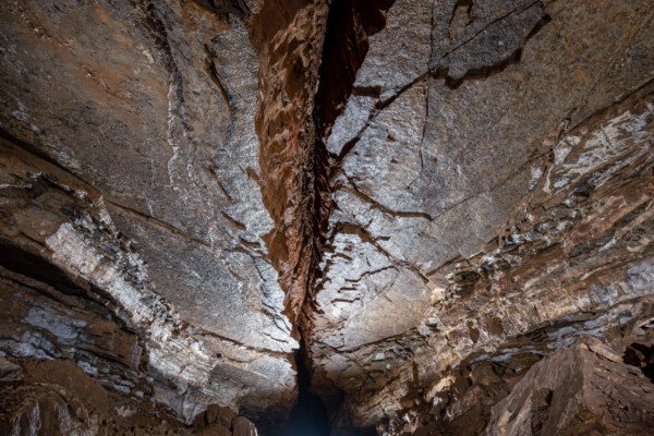 Un spéléo dans une belle galerie au plafond lisse coupé par une grosse fracture (Grotte de Pézenas, Ardèche)