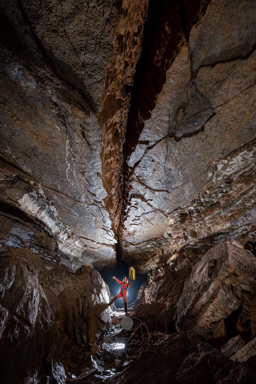 Un spéléo dans une belle galerie au plafond lisse coupé par une grosse fracture (Grotte de Pézenas, Ardèche)