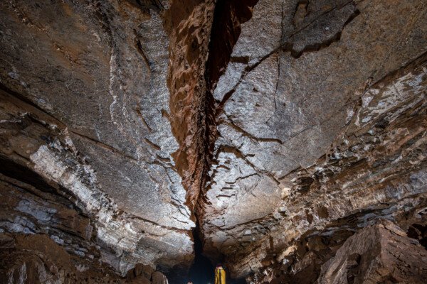 Un spéléo dans une belle galerie au plafond lisse coupé par une grosse fracture (Grotte de Pézenas, Ardèche)