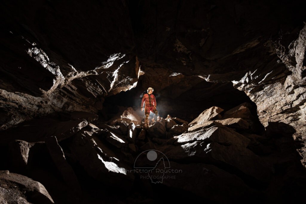 Spéléo franchissant une zone chaotique qui barre la galerie (Grotte de Pézenas, Ardèche)