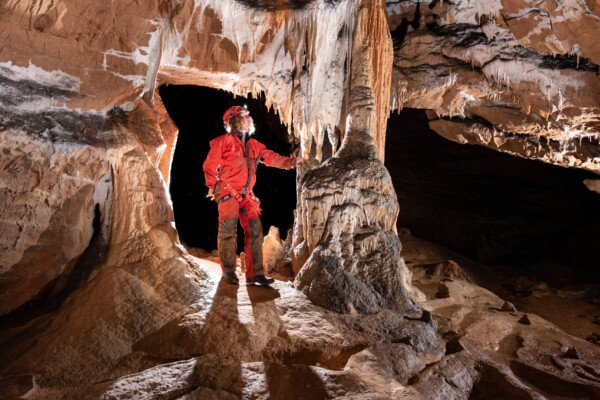 Spéléo passant entre paroi et concrétion (Grotte de la Pascaloune, Ardèche)