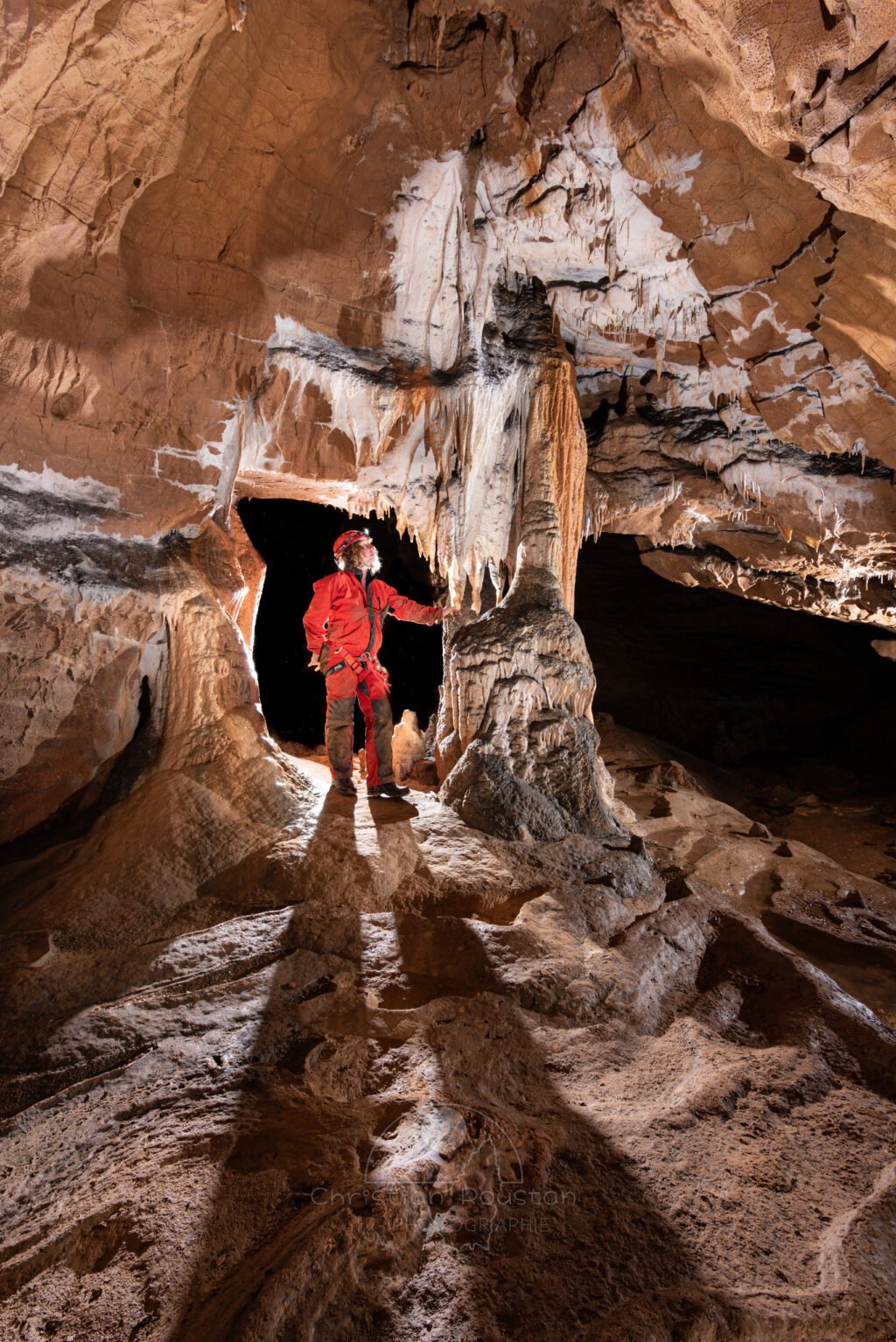 Spéléo passant entre paroi et concrétion (Grotte de la Pascaloune, Ardèche)