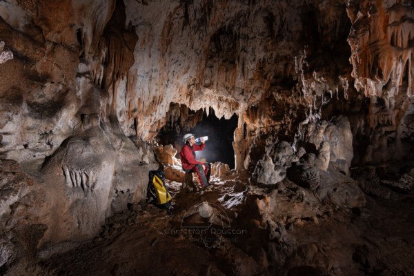 Spéléo assit dans la galerie qui boit de l'eau en bouteille (Grotte de la Pascaloune, Ardèche)