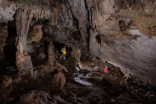 La première salle avec un spéléologue à gauche dans les concrétions et un autre tout en bas (Spéléo, Grotte du Prevel, Gard)