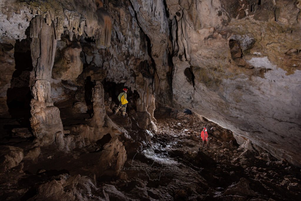 La première salle avec un spéléologue à gauche dans les concrétions et un autre tout en bas (Spéléo, Grotte du Prevel, Gard)